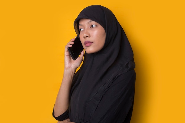 Retrato de menina muçulmana usando um smartphone em fundo amarelo
