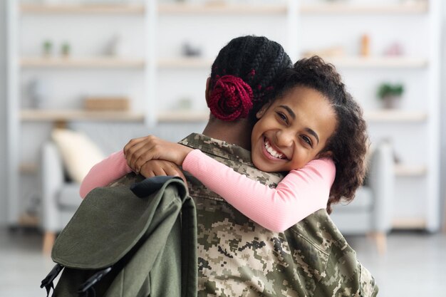 Retrato de menina negra alegre, abraçando a mãe e sorrindo