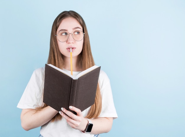 Retrato de menina pensativa pensativa com caderno e lápis na boca, olhando para longe para copyspace.