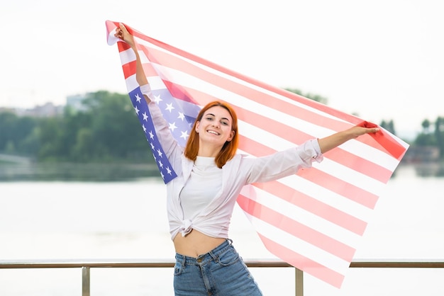 Retrato de menina ruiva sorridente feliz segurando a bandeira nacional dos EUA nas mãos Jovem positiva comemorando o dia da independência dos Estados Unidos