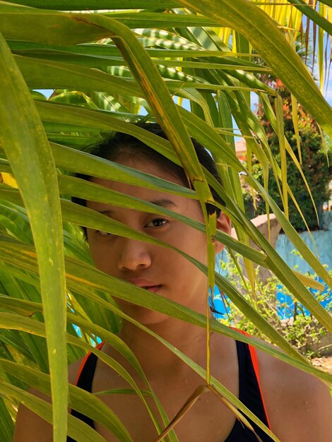 Foto retrato de menina sen através de folhas de palmeira