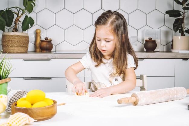 Retrato de menina séria ajudando a fazer forma massa biscoitos de páscoa Esculpir massa farinha padaria xícara biscoito Preparando rolo Prato de madeira de ovos amarelos planta Utensílio de cozinha interior