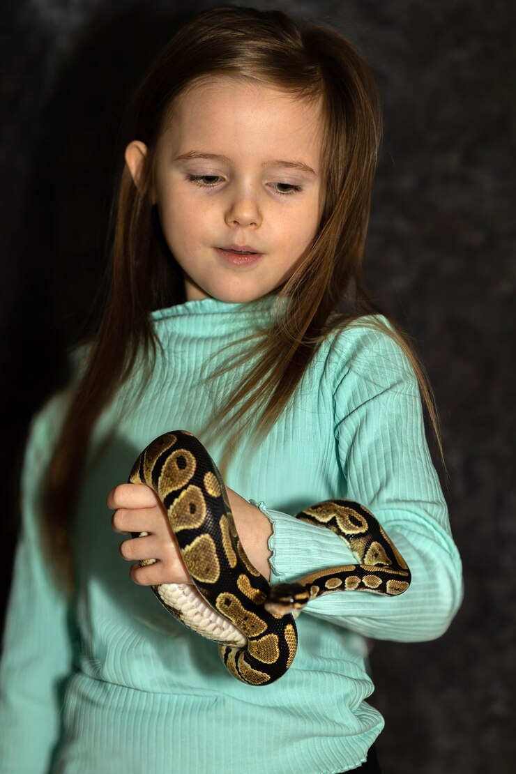 Foto retrato de menina sorridente de verde segurando uma cobra em fundo escuro