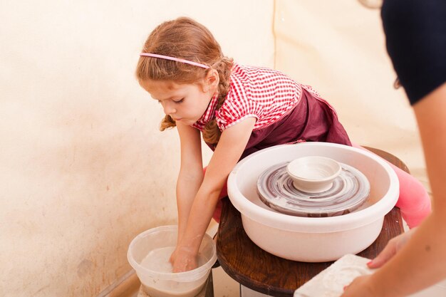 Retrato de menina tentando fazer cerâmica de argila branca em uma roda de oleiro