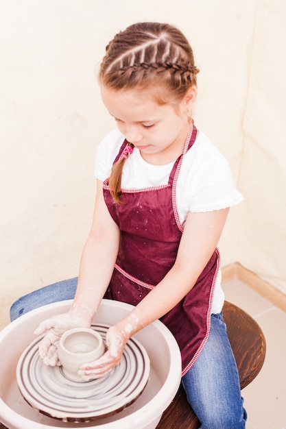 Retrato de menina tentando fazer cerâmica de argila branca em uma roda de oleiro
