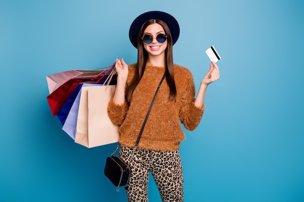 Retrato de menina turista positiva pagador de dinheiro caminhada outono inverno loja shopping varejo segurar cartão de crédito vestir calça suéter marrom óculos de sol veludo retro vintage boné isolado parede azul