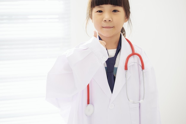 Retrato de menina vestida de médico com estetoscópio e mãos com polegares para cima