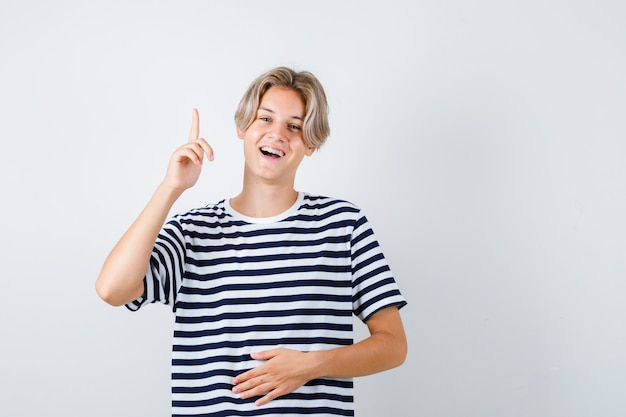 Retrato de menino adolescente apontando para cima em uma camiseta e olhando alegre para a frente