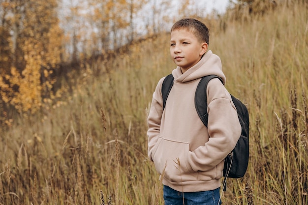 Retrato de menino adolescente sorridente com mochila andando no parque outono Estilo de vida ativo De volta à escola Menino turista na floresta de outono Foco seletivo