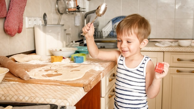 Retrato de menino alegre e sorridente feliz cozinhando e assando na cozinha em casa