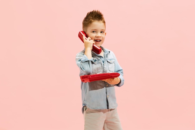 Retrato de menino alegre posando falando no telefone vintage isolado sobre o fundo rosa do estúdio