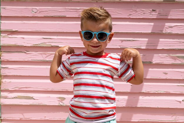 Foto retrato de menino biracial feliz sorrindo e mostrando músculos sobre parede rosa. passar tempo de qualidade, estilo de vida, infância, verão e conceito de férias.