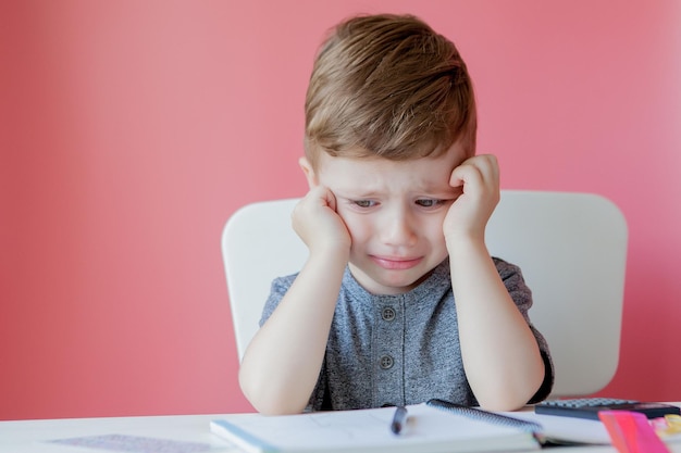 Retrato de menino bonitinho em casa fazendo lição de casa criança concentrada escrevendo com lápis colorido dentro de casa ensino fundamental e educação criança aprendendo a escrever letras e números