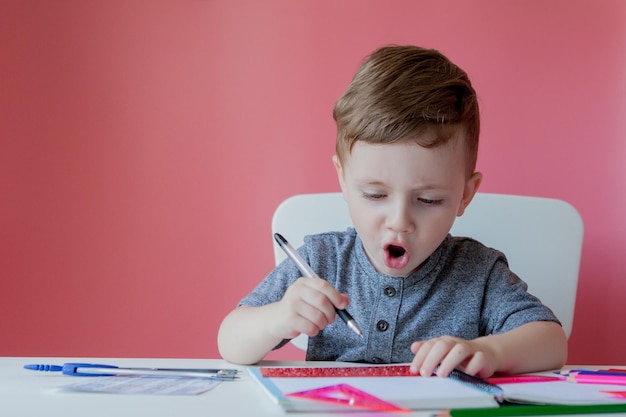 Retrato de menino bonitinho em casa fazendo lição de casa criança concentrada escrevendo com lápis colorido dentro de casa ensino fundamental e educação criança aprendendo a escrever letras e números