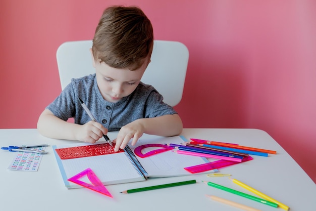 Retrato de menino bonitinho em casa fazendo lição de casa Criança concentrada escrevendo com lápis colorido dentro de casa Ensino fundamental e educação Criança aprendendo a escrever letras e números