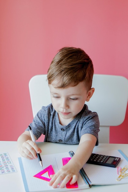 Retrato de menino bonitinho em casa fazendo lição de casa Criança concentrada escrevendo com lápis colorido dentro de casa Ensino fundamental e educação Criança aprendendo a escrever letras e números