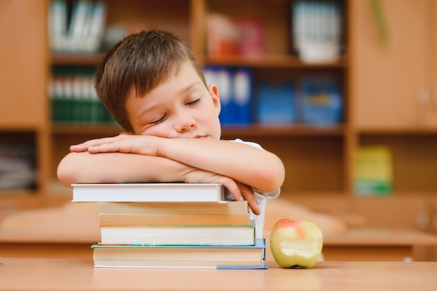 Retrato de menino bonito no topo da pilha de livros. O conceito de aprendizagem na escola primária.