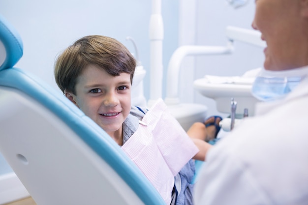 Retrato de menino bonito sentado na cadeira do dentista pelo dentista
