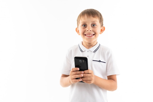 Retrato de menino caucasiano feliz conversando com seus amigos ou jogando jogos de telefone, vitórias e sorrisos