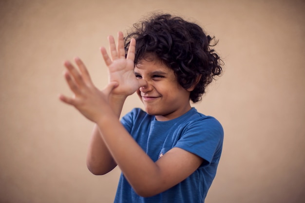 Retrato de menino criança feliz com cabelos cacheados, mostrando o gesto de provocação. conceito de crianças e emoções