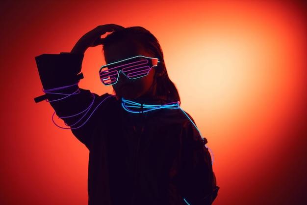 Retrato de menino cyberpunk em óculos neon em tons de azul e vermelho com fios em um fundo vermelho