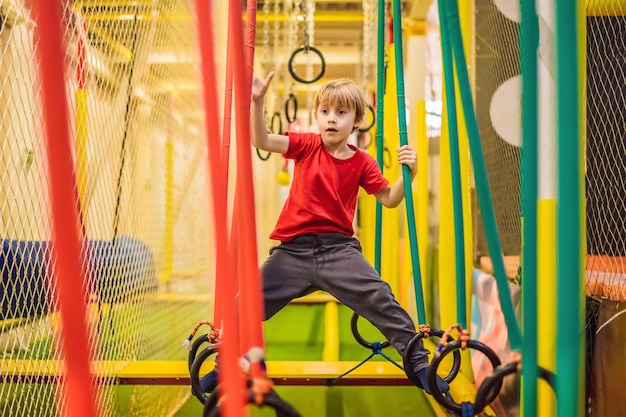 Retrato de menino de 6 anos usando capacete e escalando Criança em pista de abstáculos no playground de aventura