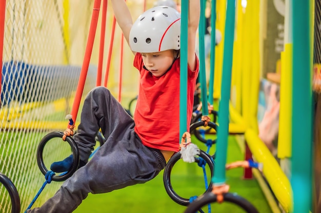 Retrato de menino de 6 anos usando capacete e escalando Criança em pista de abstáculos no playground de aventura