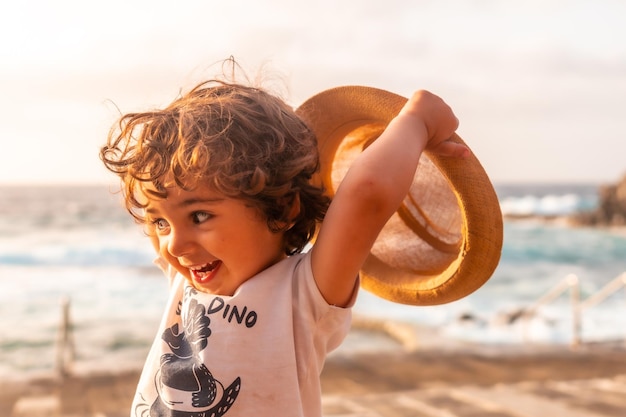 Retrato de menino de chapéu sorrindo ao pôr do sol de verão nas férias de verão na praia