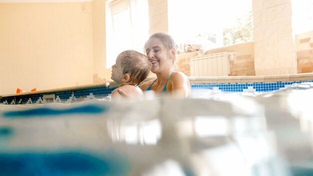 Retrato de menino de criança de 3 anos de idade com a jovem mãe nadando na piscina coberta. criança aprendendo a nadar e praticar esportes. família curtindo e se divertindo na água