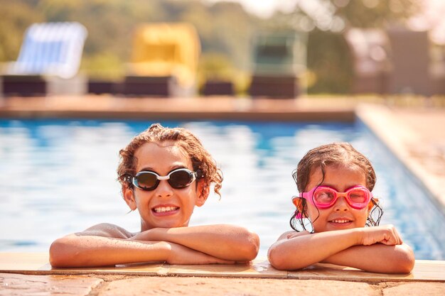 Retrato de menino e menina inclinando-se na beira da piscina nas férias de verão