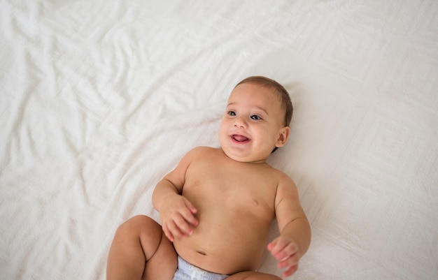 Retrato de menino feliz deitado em uma fralda em uma cama branca