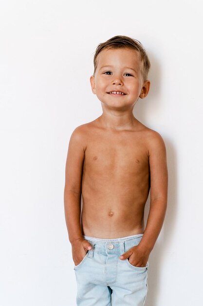 Foto retrato de menino feliz e alegre, vestindo jeans, posando contra uma parede branca