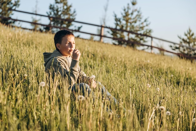 Retrato de menino feliz sentado no topo da colina no campo de grama e apreciando a bela paisagem ao pôr do sol Alpinista adolescente descansando na natureza Estilo de vida ativo Conceito de viagens locais