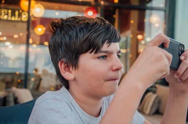 Retrato de menino jogando jogos de celular em um bar com expressão concentrada