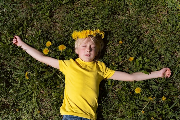 Retrato de menino loiro em camiseta amarela deitado na grama com os olhos fechados Criança dorme no gramado verde ou prado