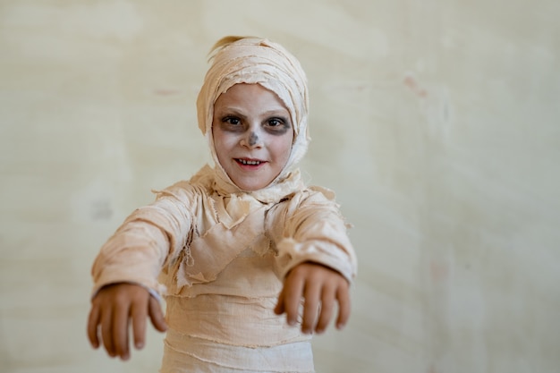 Retrato de menino positivo fantasiado de múmia feito de bandagens agindo como zumbi na festa de halloween