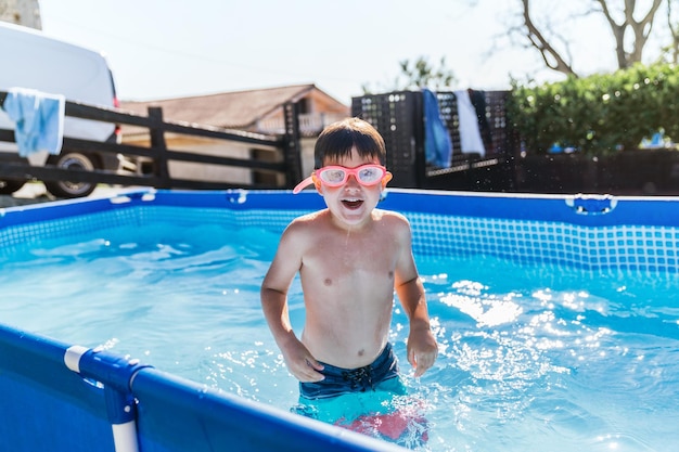 Retrato de menino se divertindo em uma pequena piscina destacável de uma casa com óculos de água