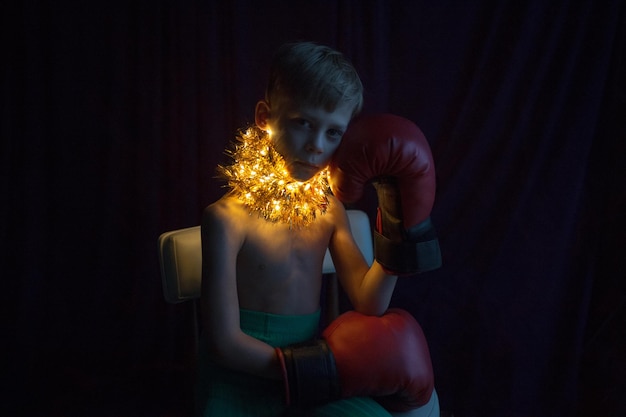 Retrato de menino sem camisa com luvas de boxe e luzes iluminadas ao redor do pescoço em casa