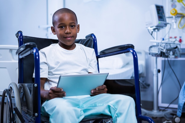 Retrato de menino sentado na cadeira de rodas com tablet digital na ala