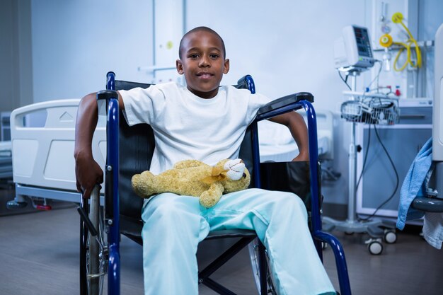 Retrato de menino sentado na cadeira de rodas com ursinho de pelúcia na enfermaria