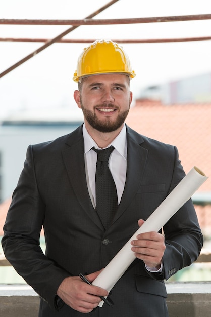 Retrato de mestre de construção com capacete amarelo e planta nas mãos