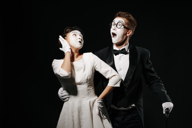 Foto retrato de mímica de casal surpreso sobre fundo preto. homem de smoking e óculos e mulher de vestido branco