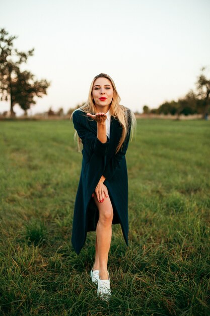 Retrato de moda ao ar livre, estilo de vida, de uma garota loira deslumbrante feliz sorrindo e beijando a câmera