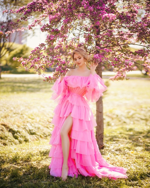 Retrato de moda arte de uma bela jovem loira em um jardim de primavera rosa florescendo em um vestido longo rosa como uma princesa em conto de fadas