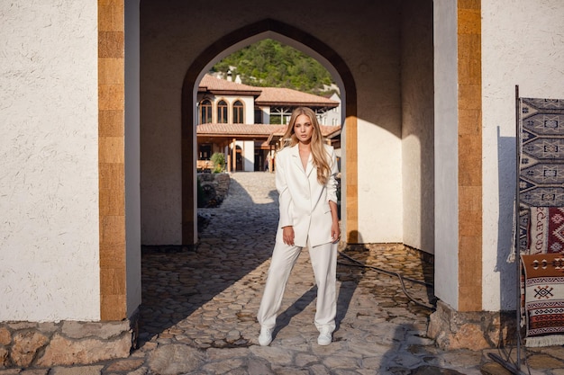 Retrato de moda de corpo inteiro ao ar livre de uma mulher elegante de terno branco posando na rua da cidade do leste Bela foto elegante de uma loira bronzeada para uma revista de moda