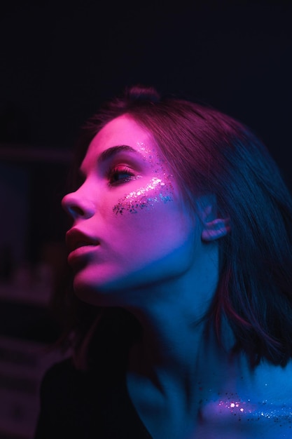 Retrato de moda de uma mulher com maquiagem brilhante com glitter em luz colorida em um quarto escuro