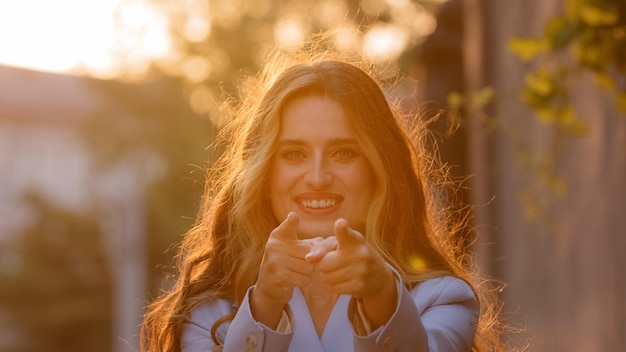 Retrato de modelo feminino fica na rua à luz do sol por do sol feliz sorridente mulher menina olhando para a câmera faz gesto ei você mãos pistolas aponta dedos indicadores direção concordando fingindo tiro