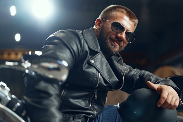 Retrato de motociclista homem barbudo em óculos de sol escuros em fundo escuro