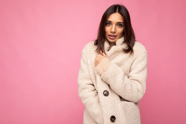 Foto retrato de muito encantador autoconfiante bonito elegante jovem morena feminina vestindo casaco quente de beaige outono isolado no fundo rosa com espaço de cópia e sensação de frio.