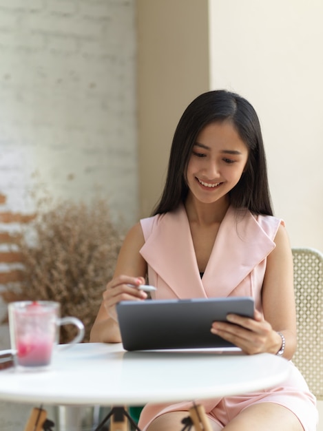 Retrato de mulher adolescente relaxando com tablet digital e bebida na mesa de café no café